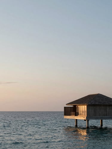 Extreme wide environmental shot of a single minimalist overwater villa against an empty horizon at twilight, soft low-angle golden hour lighting, calm ocean, negative space on the left.