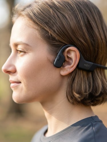 Close-up profile shot of an individual wearing the open-ear headset, showing the device resting behind the ear without covering the ear canal, bright natural morning light, shallow depth of field, 50mm lens