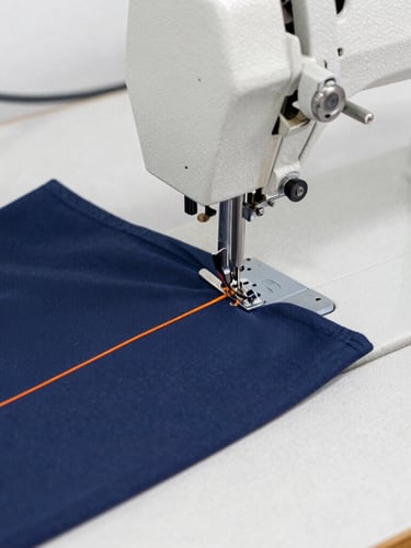 Crisp industrial photography, close-up macro shot of a heavy-duty sewing machine stitching a navy blue corporate uniform with bright orange thread, sharp focus on needle, clean workshop background