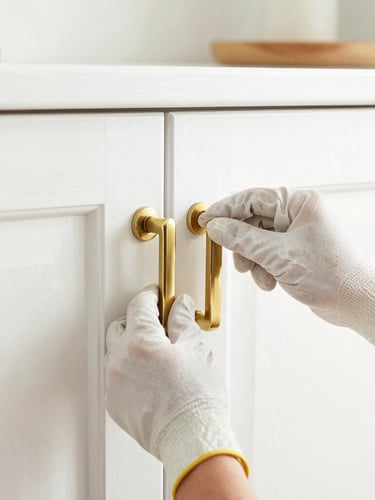 Close-up of hands wearing clean work gloves carefully adjusting a newly installed brass cabinet pull, bright natural daylight, pristine finished white wood, soft gold accents, 35mm lens.