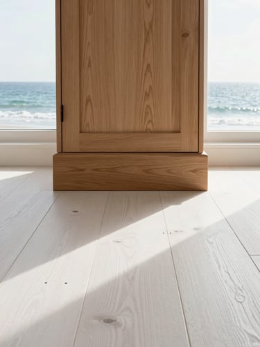 Straight-on architectural shot of restored historical white oak flooring meeting a custom-built cabinet base. Bright, natural coastal daylight streams through a nearby window, highlighting the rich grain of the wood and the clean, precise joinery. Level, centered framing emphasizing symmetry and order.