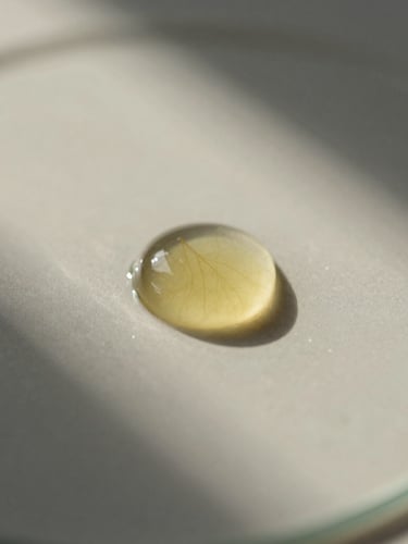 Macro close-up of pure botanical oil droplets on a clean glass surface under soft morning light, warm shadows, minimalist composition.