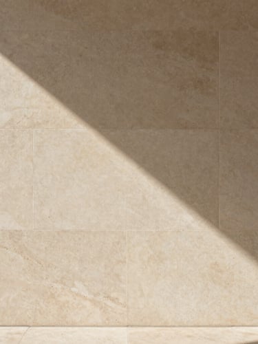 Plano de detalle de un muro de piedra caliza texturizada y hormigón pulido, sombras suaves y geométricas proyectadas de forma natural, estética editorial minimalista.