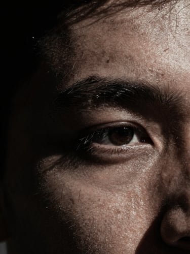 Macro crop of a man's brow and eye in deep shadow, sharp focus, geometric lines, desaturated charcoal tones, dramatic low-key lighting, 35mm.