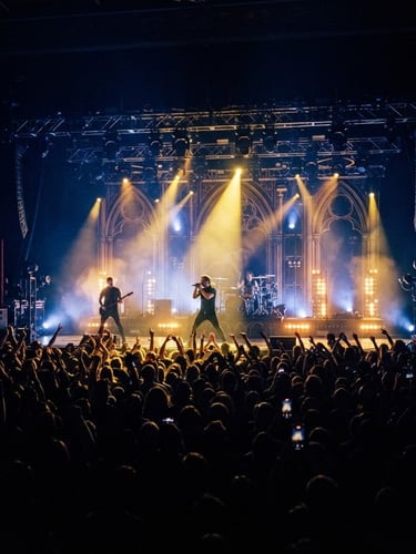 Dramatic wide-angle shot of an illuminated concert stage with deep navy and gold lighting, crowd silhouettes in the foreground, 35mm