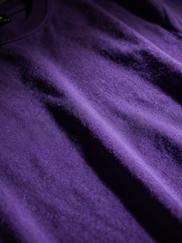 Close-up of premium heavy-weight violet cotton fabric with high-contrast shadows, embroidered details visible under harsh overhead light