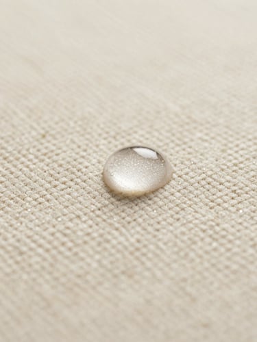 Macro close-up of clear liquid beading perfectly on a highly textured cream bouclé fabric, soft diffused side lighting highlighting the weave, minimalist and clinical luxury feel.