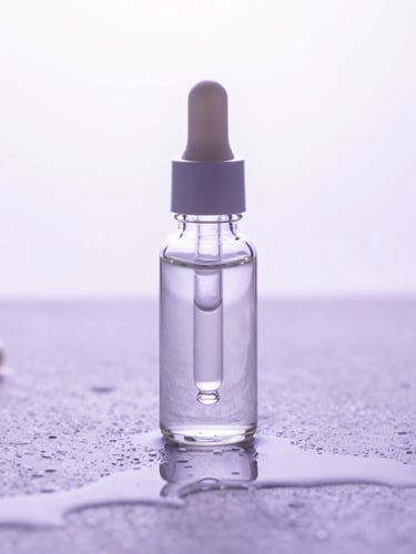 A clean glass dropper bottle reflecting bright studio light on a wet stone surface with soft lavender reflections, clinical macro framing.