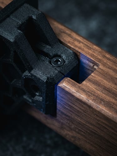 Extreme macro studio photograph of a matte black 3D-printed bracket interlocking with a solid walnut joint, moody directional lighting with a subtle blue LED glow, high contrast.