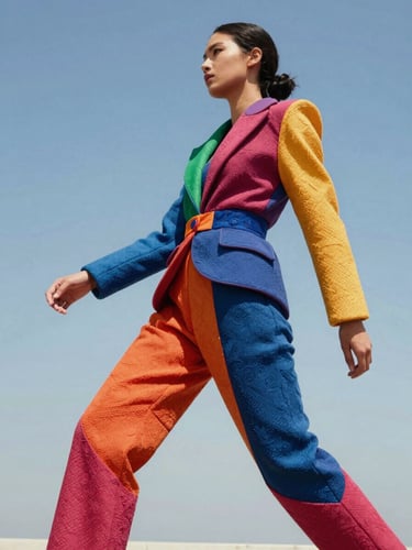 Vibrant editorial fashion photography, bright natural sunlight, a model in dynamic motion wearing a bold, sculptural custom outfit with rich textures, high contrast, 35mm lens.