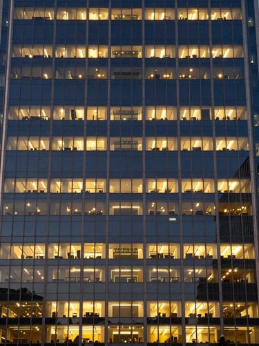 Straight-on elevation of a modern glass and steel office skyscraper at dusk, warm interior lights glowing, architectural symmetry, medium format