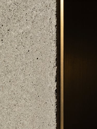 Extreme macro detail of modern textured board-formed concrete meeting a sharp bronze architectural trim, dramatic low-key chiaroscuro lighting.