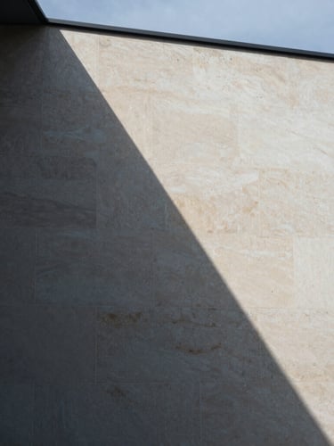 A close-up architectural crop of sharp geometric shadows falling across a warm alabaster limestone facade, cool overcast daylight, 35mm editorial photography.
