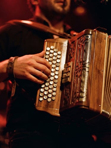 Close-up of a polished wooden accordion being played under dramatic warm stage lights, rich crimson tones, shallow depth of field
