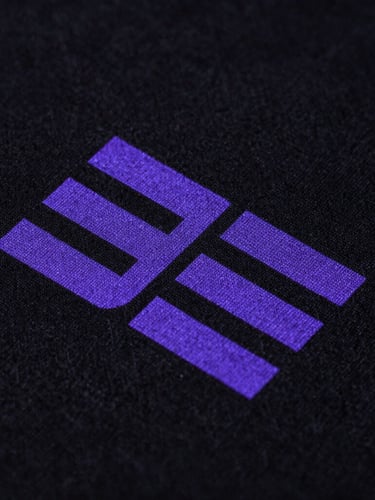 Macro extreme close-up shot of high-density neon purple ink printed on a black heavyweight organic cotton fabric texture, showing the intricate weave and clean print edges, dramatic studio lighting.