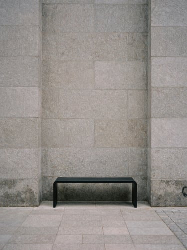 Architectural detail of a quiet Copenhagen courtyard, soft overcast light, textured gray stone walls, a single minimalist black metal bench, desaturated tones, 35mm film grain.