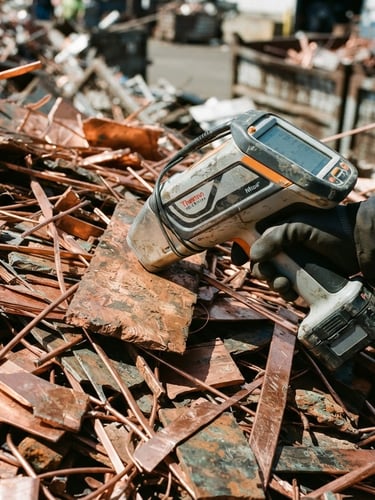 A close-up of a handheld XRF analyzer being pressed against sorted copper scrap, harsh direct daylight, high-contrast metallic tones, sharp focus, 35mm
