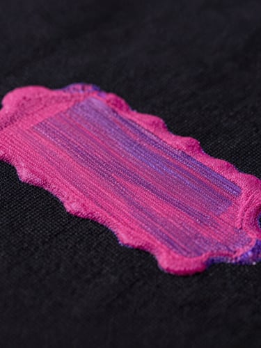 Extreme close-up of vibrant magenta ink layers drying on a heavy black cotton fabric, sharp studio lighting with subtle purple gel accents, macro detail, 50mm