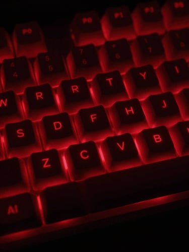 Extreme close-up of a mechanical keyboard glowing under intense crimson red backlighting, heavy dark shadows, low-key dramatic lighting, 35mm lens, raw low-key gaming aesthetic.