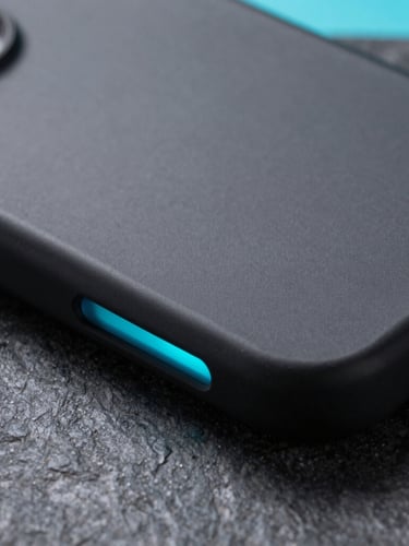 Extreme close-up of a premium matte black phone case on a dark stone surface, sharp edges, illuminated by a sharp neon cyan side-light, macro photography.