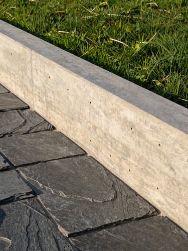 Close-up of a sharp, modern concrete retaining wall meeting natural slate stone, crisp afternoon golden hour light, high contrast
