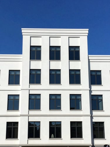 Straight-on architectural shot of a clean modern commercial building, bright midday sun, deep blue sky, professional soft-wash rig visible in the lower right third, 35mm.