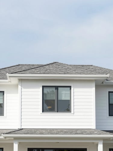 Straight-on architectural crop of a pristine modern home with clean slate roof shingles and crisp white siding under bright overcast daylight, high contrast, 35mm