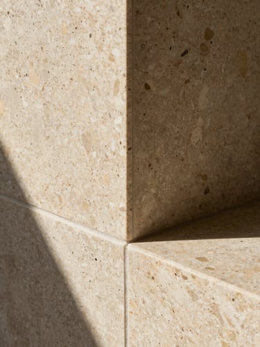 Close-up of premium warm travertine stone meeting raw textured concrete, dramatic natural light, sharp architectural shadows, luxury architectural photography
