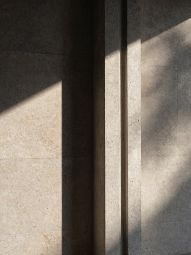 A vertical medium format photograph of a modern concrete column meeting a travertine wall, dramatic sunlight casting sharp geometric shadows, architectural detail
