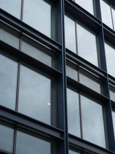 Extreme close-up of structured architectural steel and glass facade, overcast daylight, deep navy tones, sharp lines, 35mm
