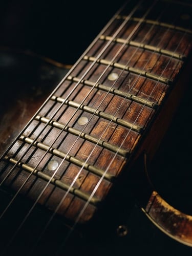 Moody high-contrast close-up of a worn electric guitar neck and brass frets, dramatic side-lighting, rich warm wood tones, deep shadows, analog film grain, 50mm