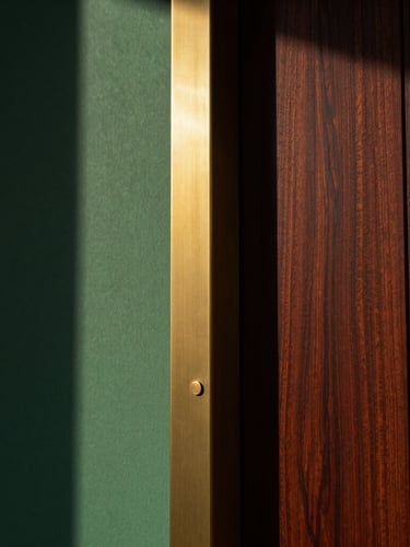 Editorial architectural photography of a premium material transition, brushed brass meeting dark walnut wood, low-angle golden hour light casting deep shadows, 35mm.