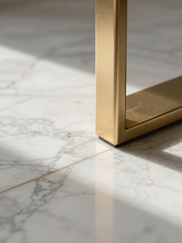 Extreme close-up of Italian marble flooring meeting a champagne-gold bespoke fixture, crisp morning light highlighting the premium materials.