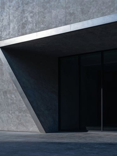 Sweeping architectural perspective of a minimalist concrete and dark glass structure, sharp silver angles, dramatic cool directional lighting, deep indigo shadows.
