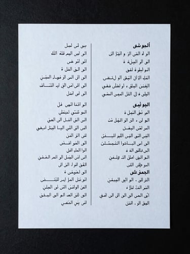 Close overhead flat-lay of a bilingual annotation worksheet, Arabic and Chinese script side by side on a dark desk surface, cool even studio light, sharp text clarity, minimal clutter