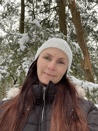 A smiling middle-aged woman standing in front of snow-covered trees.