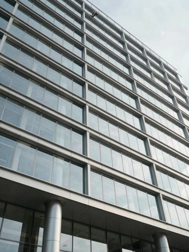 Low-angle architectural shot of a modern glass-and-steel government building facade, bright daylight, sharp structural lines.