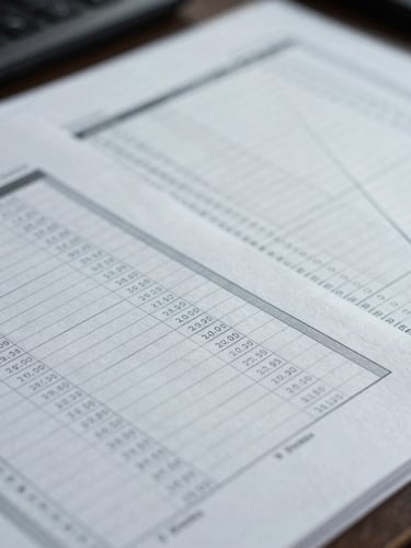Close-up of structured financial ledger sheets on a desk, cool diffused office lighting, desaturated navy and gray tones, sharp focus.