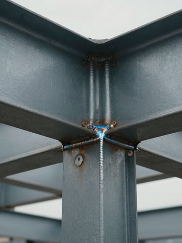 Tight architectural documentation shot of a steel beam-to-column connection joint, weld beads visible, overcast industrial lighting, no people
