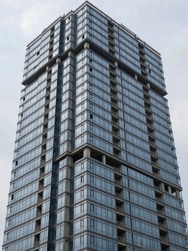 Close wide shot of a completed high-rise commercial facade, glass curtain wall meeting exposed concrete columns, overcast daylight revealing true material color, no people