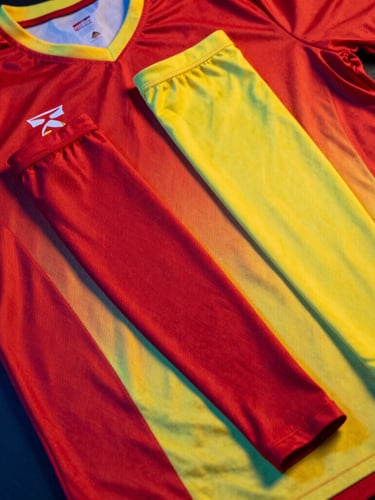 Overhead flat-lay of a matching tournament-grade jersey and compression arm sleeve set in vibrant crimson and canary yellow, high-contrast athletic studio lighting with dramatic blue rim lights reflecting off the technical fabric, sharp detail, 85mm lens