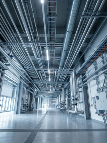 Wide-angle, low-angle shot of a modern, clean industrial facility interior with visible, precisely routed MEP conduits and pipelines along the ceiling and walls, cool industrial lighting, sharp focus, no people.