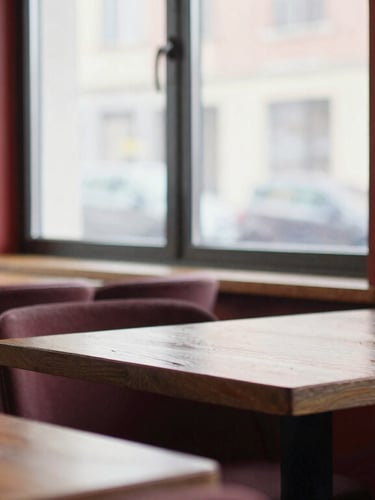 Cozy Scandinavian-style restaurant interior with empty wooden tables, warm window reflections, soft diffused natural daylight, rich crimson accents, 35mm