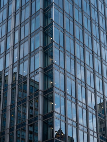 Symmetrical vertical shot of a modern glass and steel skyscraper corner, sharp blue hour reflections, kissing the left edge of the frame.