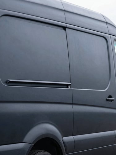 A close-up of a matte black commercial Mercedes Sprinter van, showing a flawless vinyl wrap application around the rear door hinge, sharp studio lighting, high contrast.