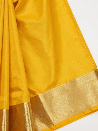 Close-up macro shot of vibrant marigold yellow silk saree fabric, showing intricate gold zari thread weaving and rich textile texture under soft daylight.