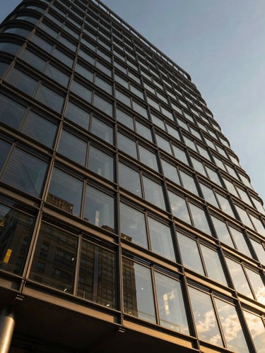 Low-angle dramatic view of a modern high-rise glass facade reflecting golden-hour sunlight, structural steel framework visible, wide lens, cinematic lighting