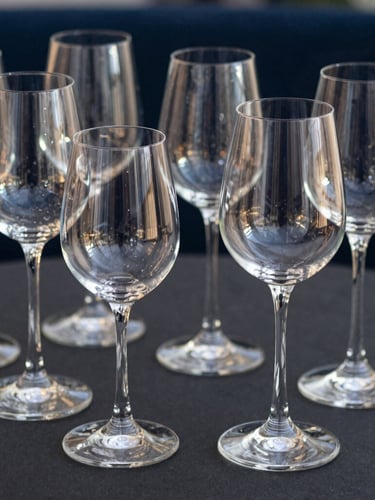 Elegant ARC stemware arranged on a dark table, sharp high-contrast reflections on the glass under focused spotlighting.