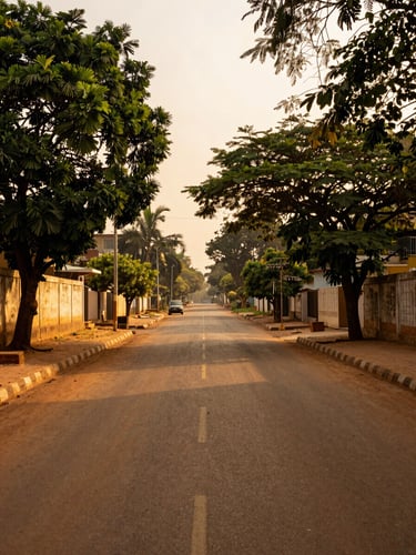 Ground-level environmental shot looking down a wide East Legon boulevard at golden hour — high compound walls with mature trees overhanging, a single parked vehicle in the far distance, warm amber light on the tarmac, no people, generous atmospheric depth