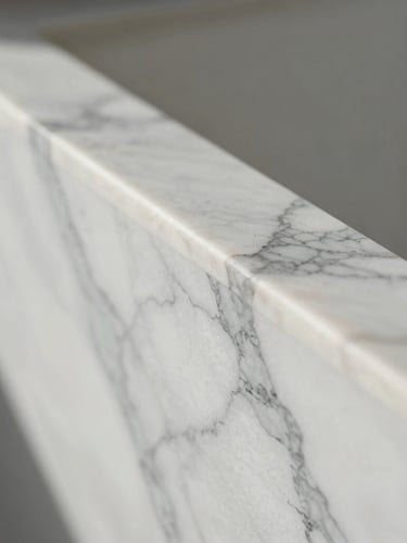 An extreme close-up portrait shot of polished white Calacatta marble with delicate grey veining, soft natural morning light catching the flawless edge.